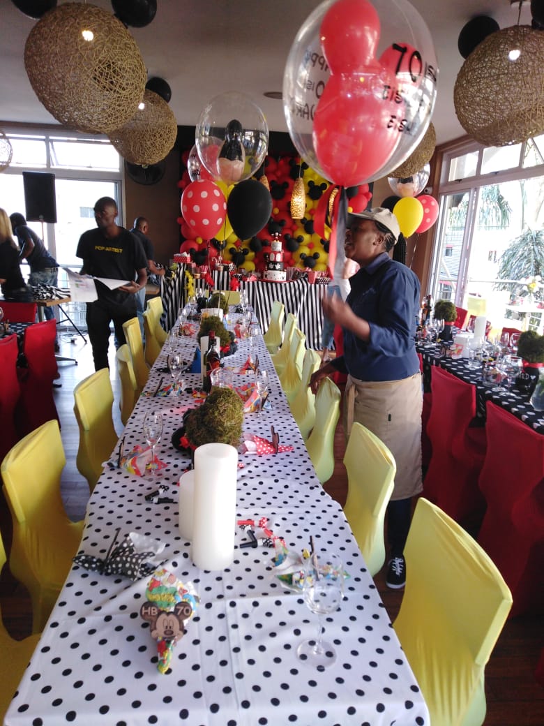 Long party table with polka dot cloths, yellow chairs and balloons