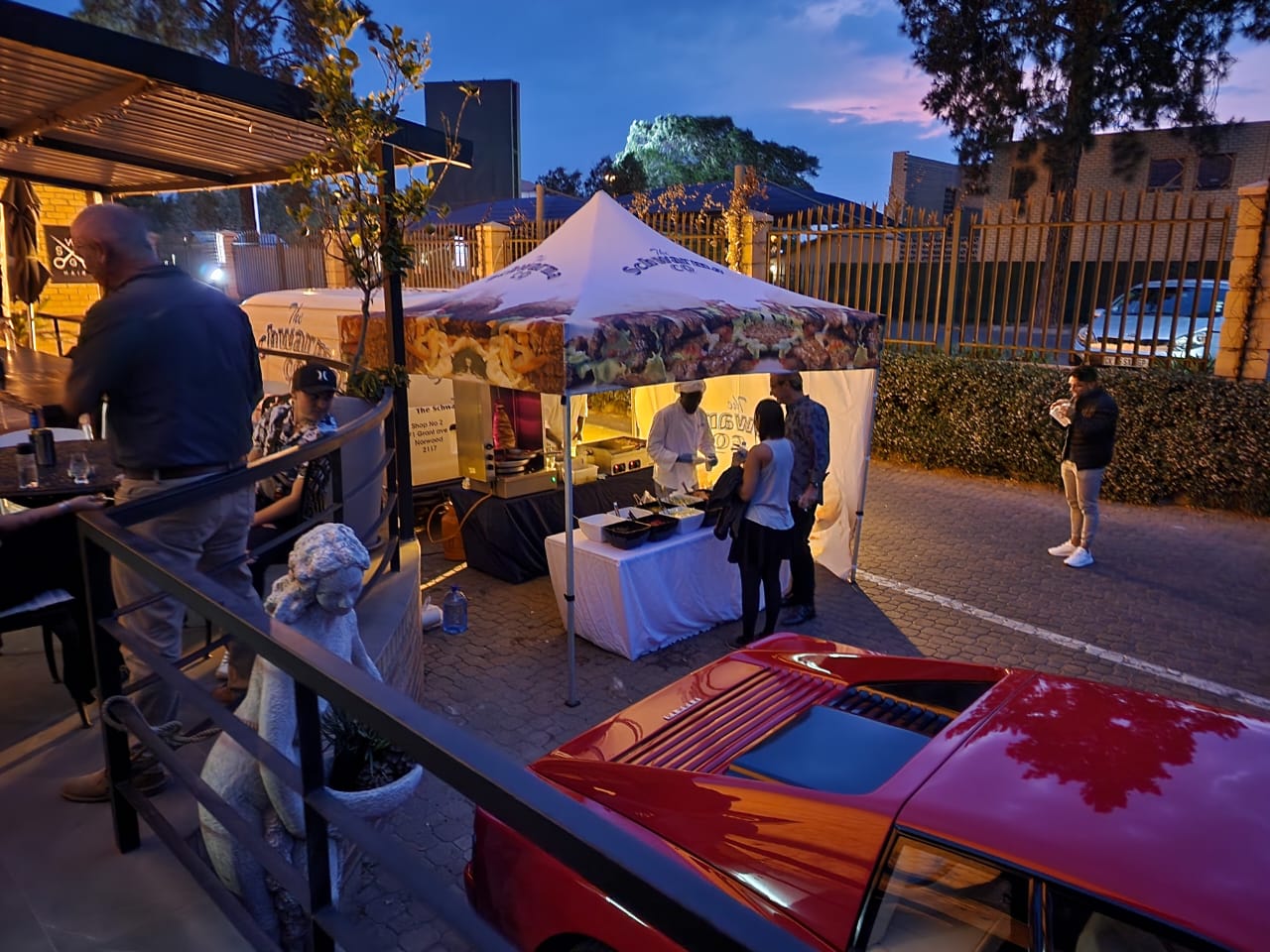 The Schwarma Company gazebo lit up at dusk, chefs serving guests